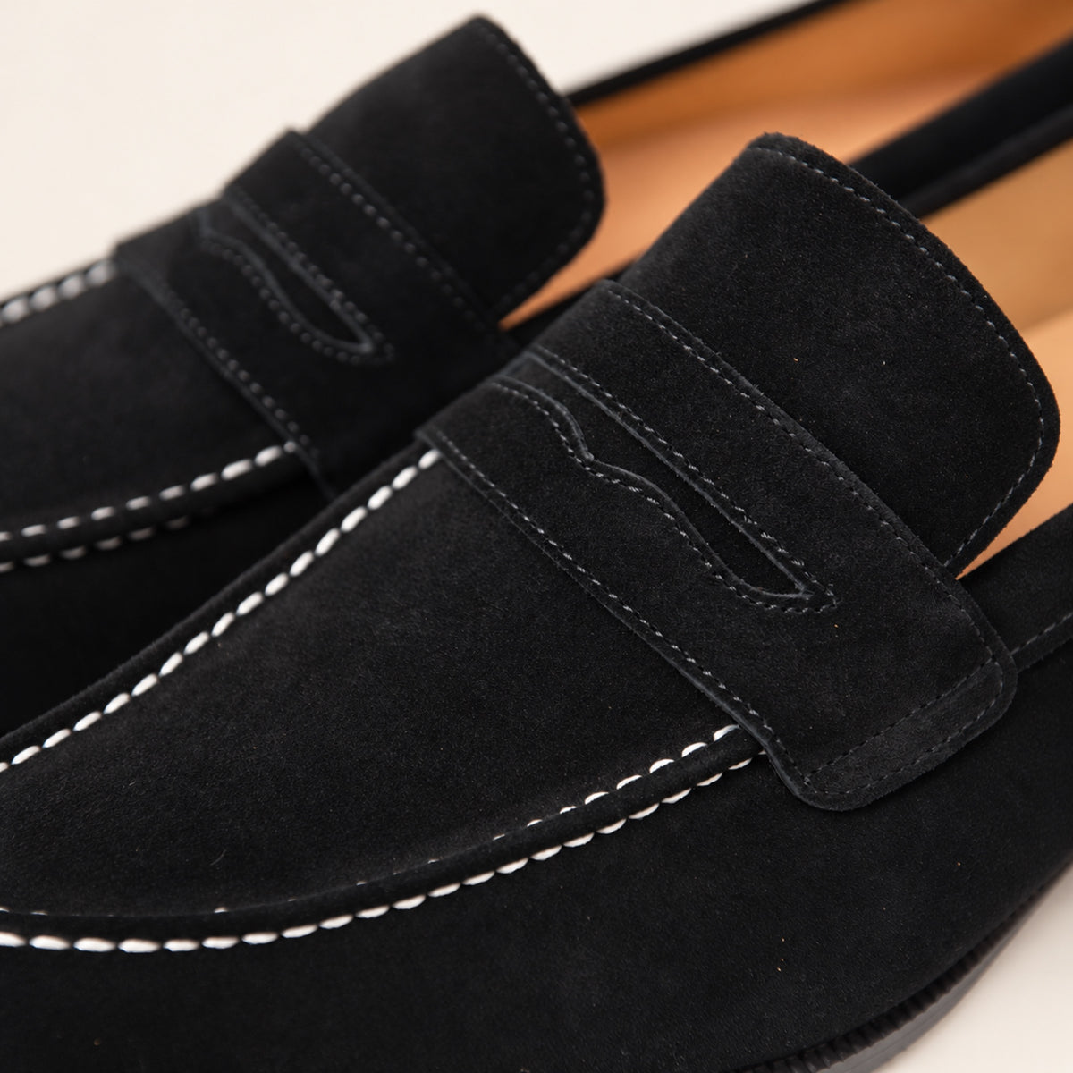 Black Suede Penny Loafers, close-up detail on an ivory studio background.