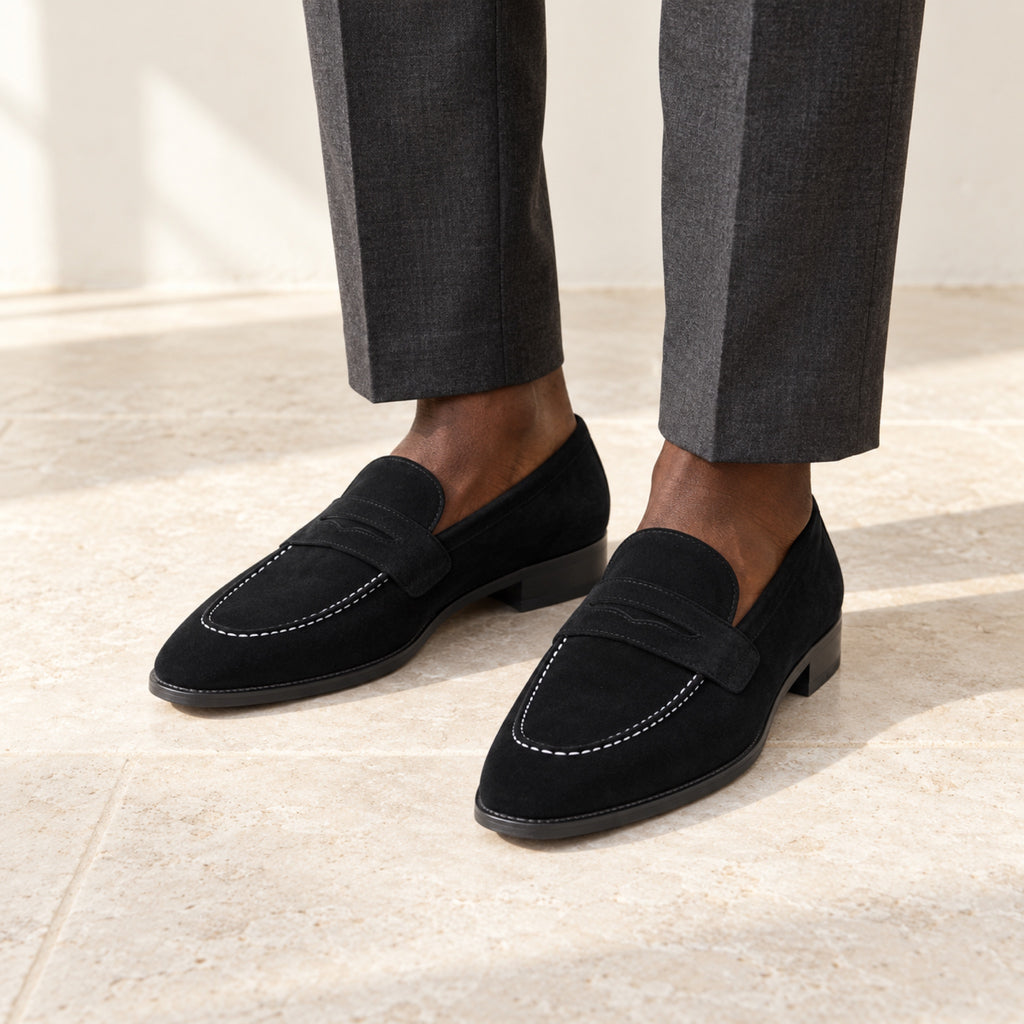 Black Suede Penny Loafers worn with tailored trousers by a model with deep brown skin, cropped below the knees.