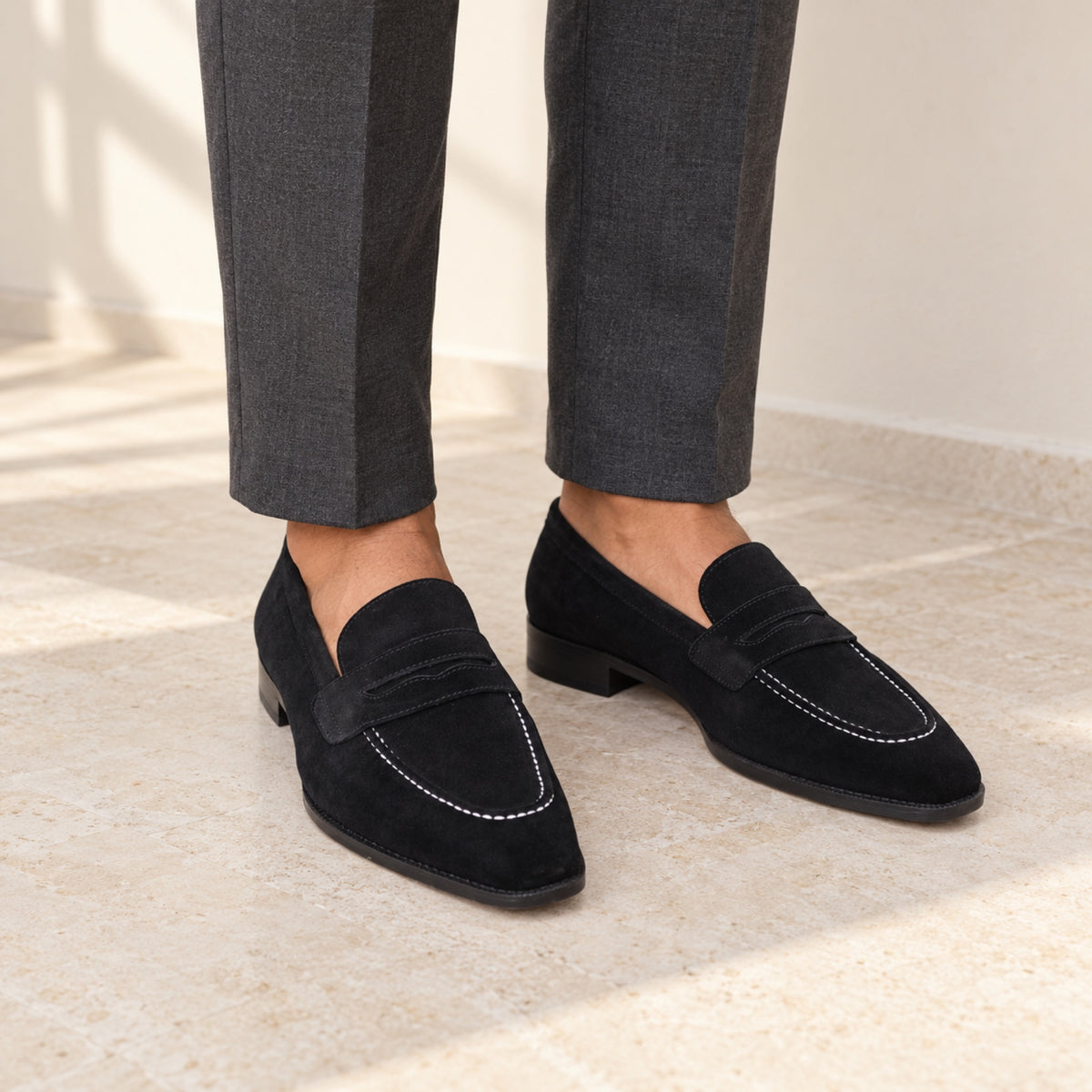 Black Suede Penny Loafers worn with tailored trousers by a model with medium brown skin, cropped below the knees.