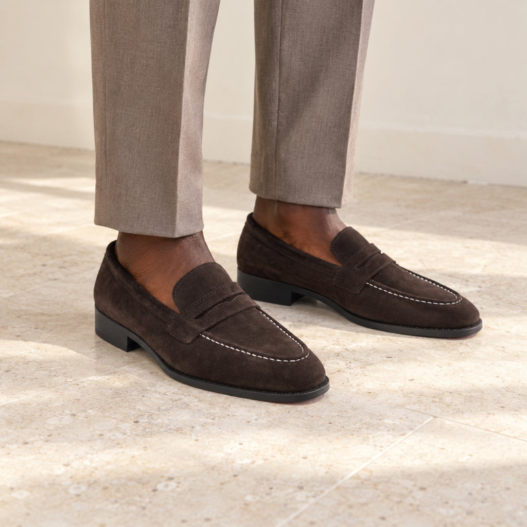 Expresso Brown Suede penny loafers worn with tailored trousers by a model with deep brown skin, cropped below the knees.